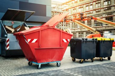 Red dumpster, recycle, waste and garbage bins near new office building. Construction site on background